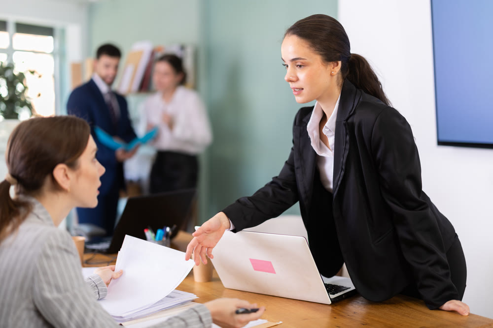 Female manager leaning over table and instructing young employee