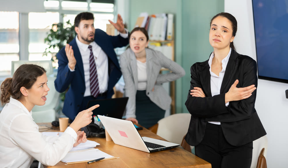 Group of people scolding sad colleague sitting at laptop in office