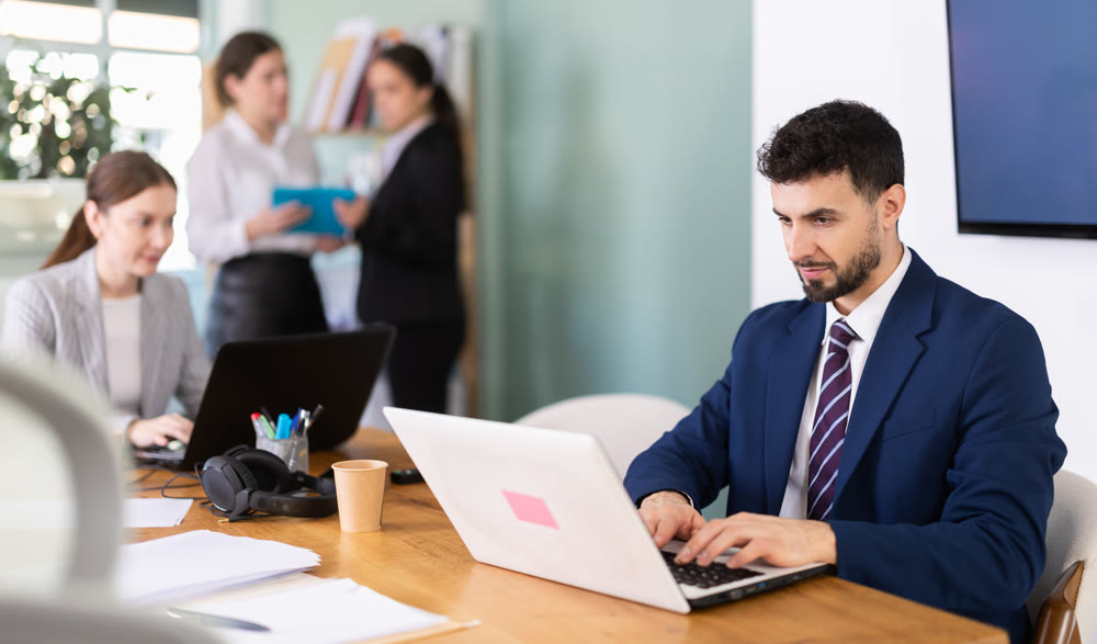 Young man works on laptop with colleagues