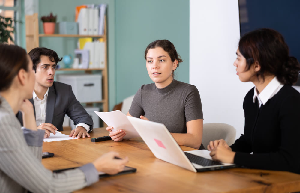 Interested office workers sitting at table with papers and laptop and discussing ideas during business meeting in office