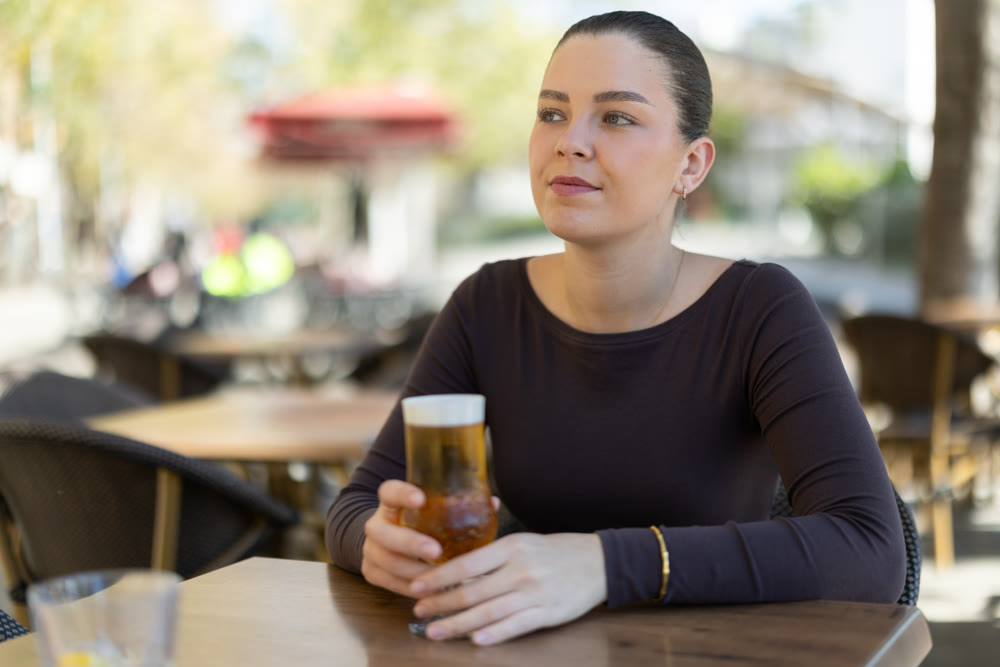 Woman drinking beer while sitting at table on cafe terrace
