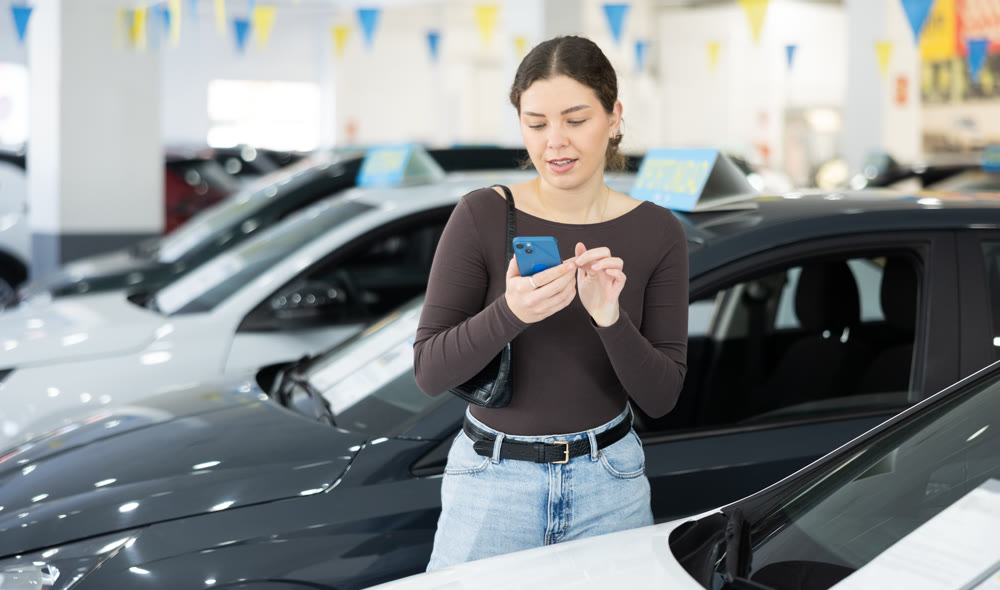 Young woman scanning QR code while choosing car at dealership
