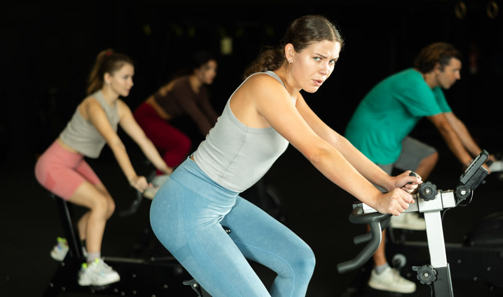 Sportive young girl doing spin bike exercises in well-equipped gym