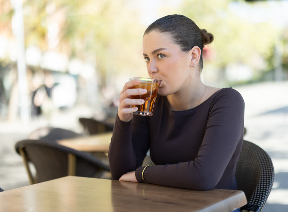 Woman drinking iced tea while sitting at table on cafe terrace