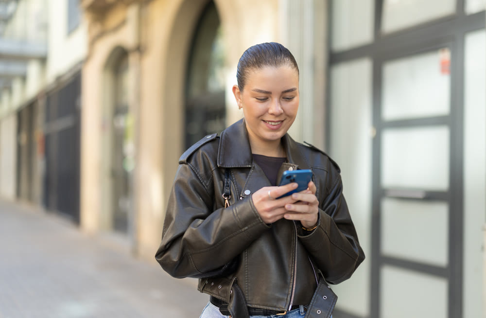 Joyful woman with a phone in hands walks around city, she looks at maps in mobile application