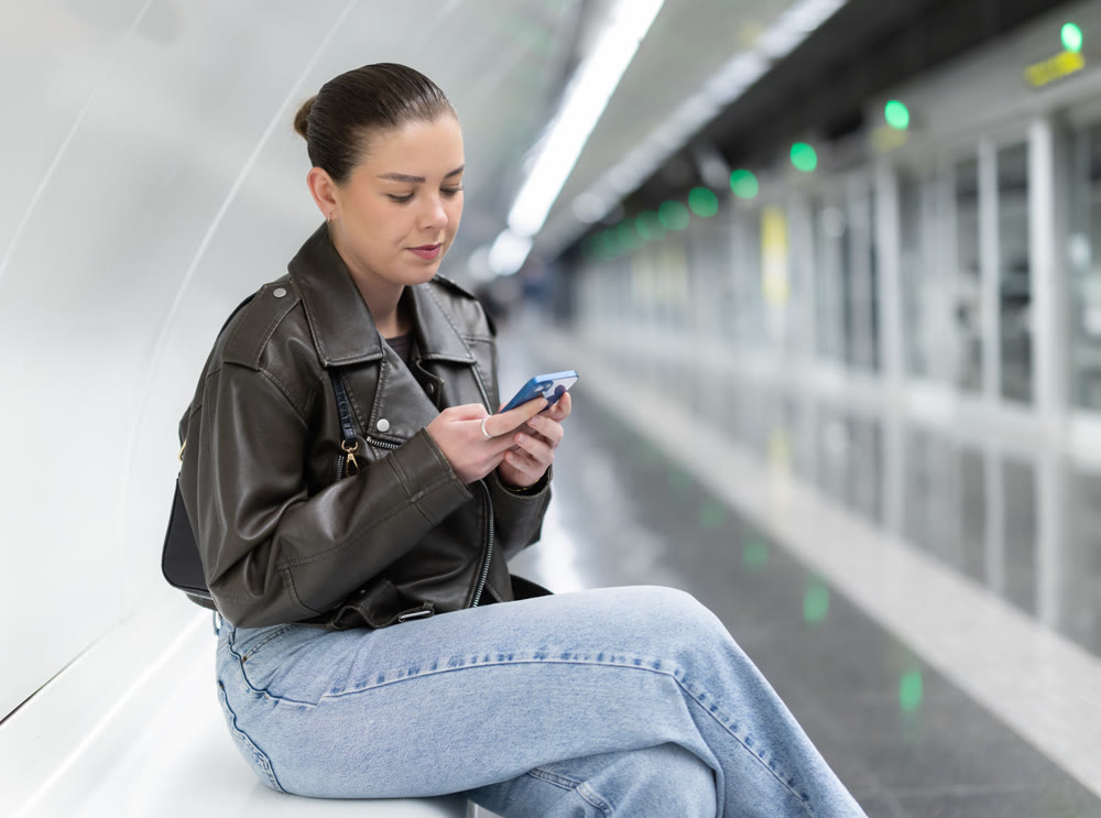 Young woman with phone sitting at metro station