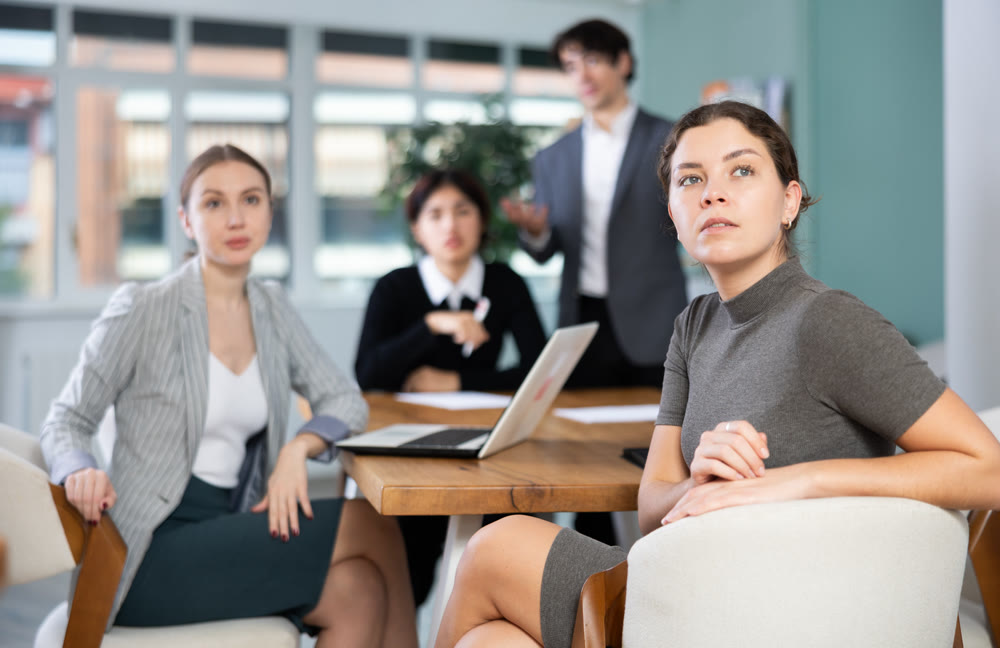 Interested malaysian girl office worker sitting at table with group of people and watching presentation during business meeting in office