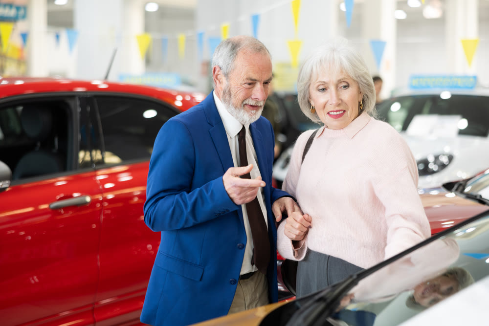salesman shows a car to an elderly woman at a car dealership
