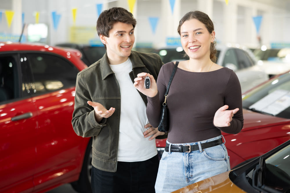 Young couple holding keys to new car in dealership
