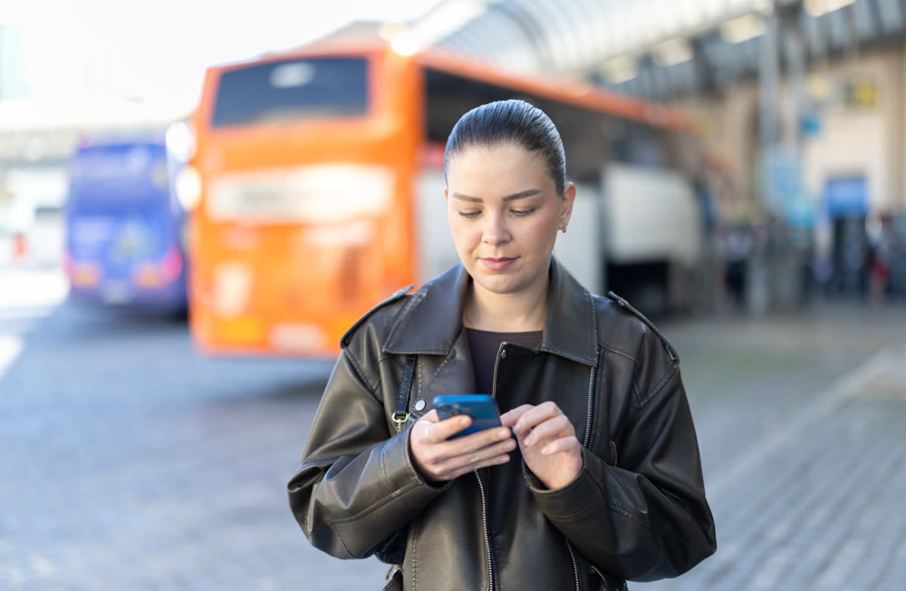 Young woman standing at transport stop with phone