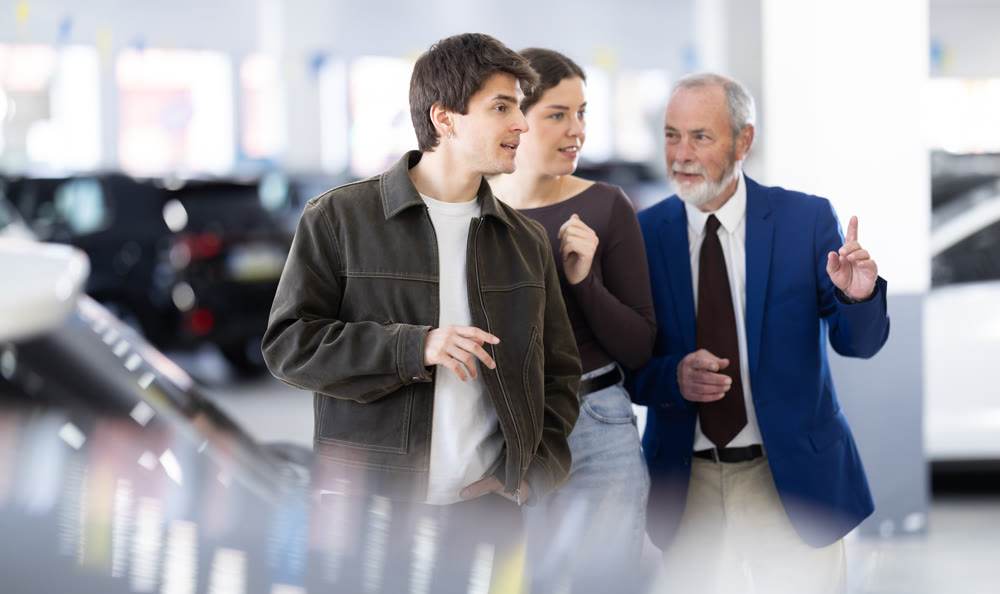 Senior salesman advises a young couple at a car dealership