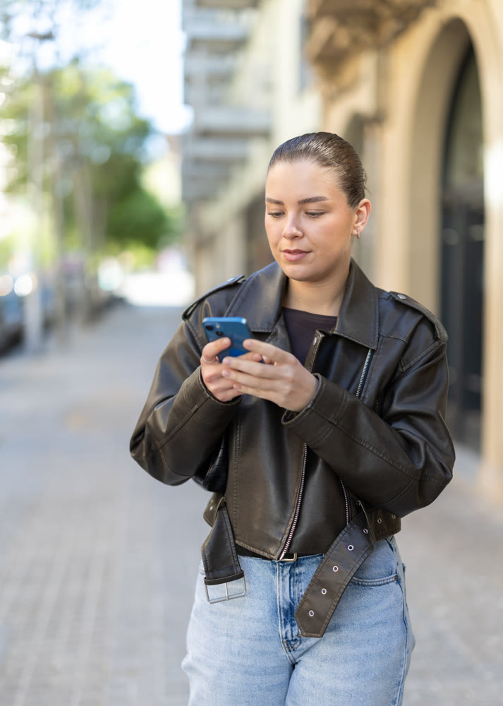 Joyful woman with a phone in hands walks around city, she looks at maps in mobile application