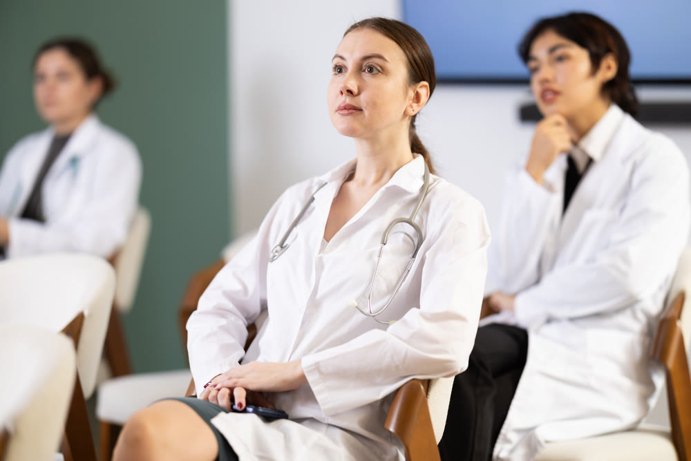 Young female doctor listening and taking notes in lecture hall