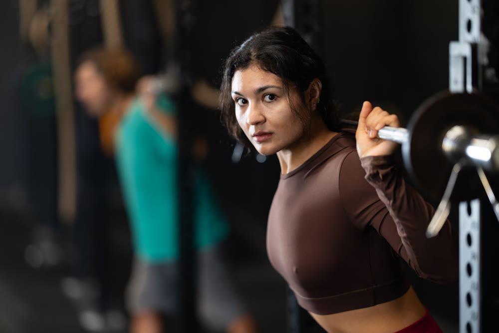 Sportive Latina girl lifting barbell in sports hall