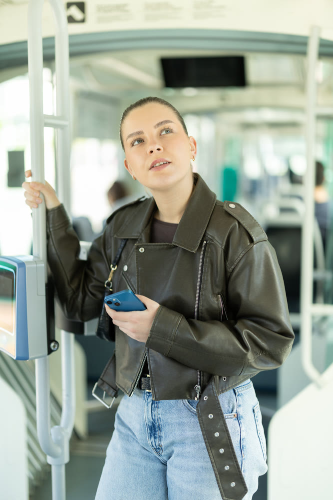 Positive woman is standing in tram wagon with phone. Girl whiles away time on trip communicating on social networks