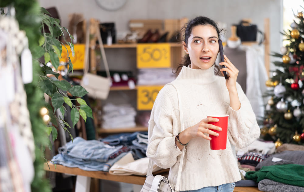 Armenian girl with cup of coffee talking on phone in womens clothing store