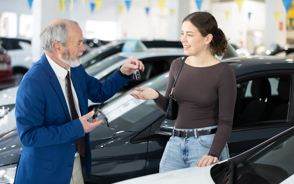Elderly salesman selling car to young woman at dealership