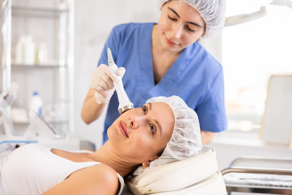 Young female cosmetologist doing ultrasound procedure to young woman