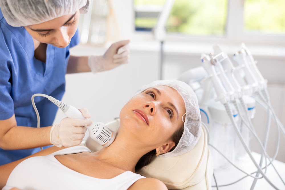 Young female cosmetologist performing neck whitening procedure on young woman
