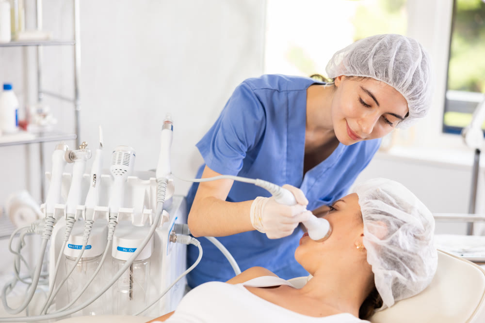 Young female cosmetologist doing ultrasound procedure to young woman