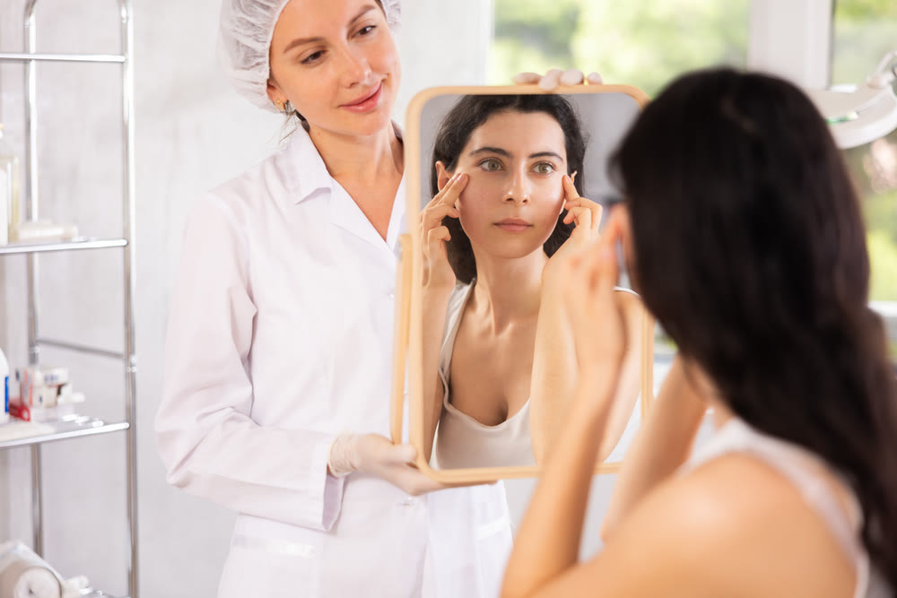 Young woman scrutinizing her reflection in mirror alongside cosmetic expert