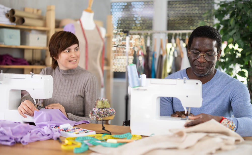 Male and female dressmakers stitching at machines in sewing workshop