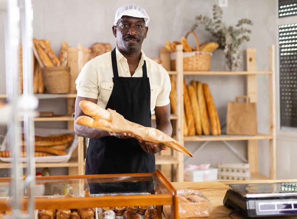 Portrait of male baker with bread and baguettes in hands in bakery
