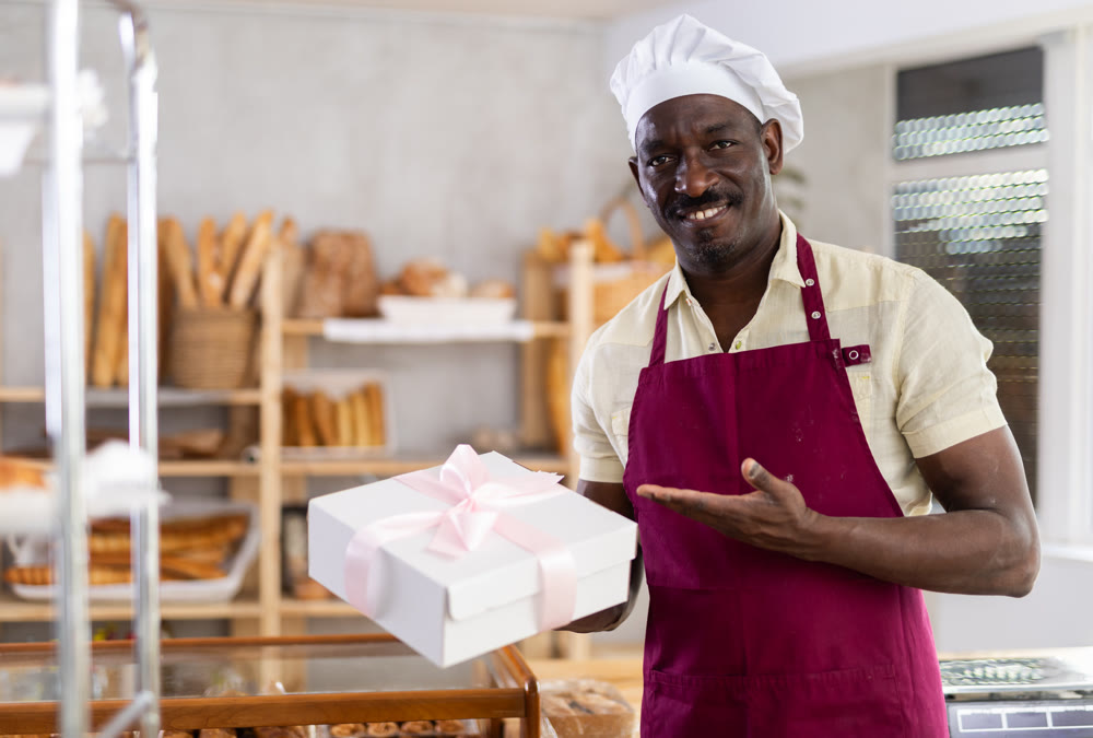 African American man entrepreneur owner of bakery holds out paper bag with pastries in hand