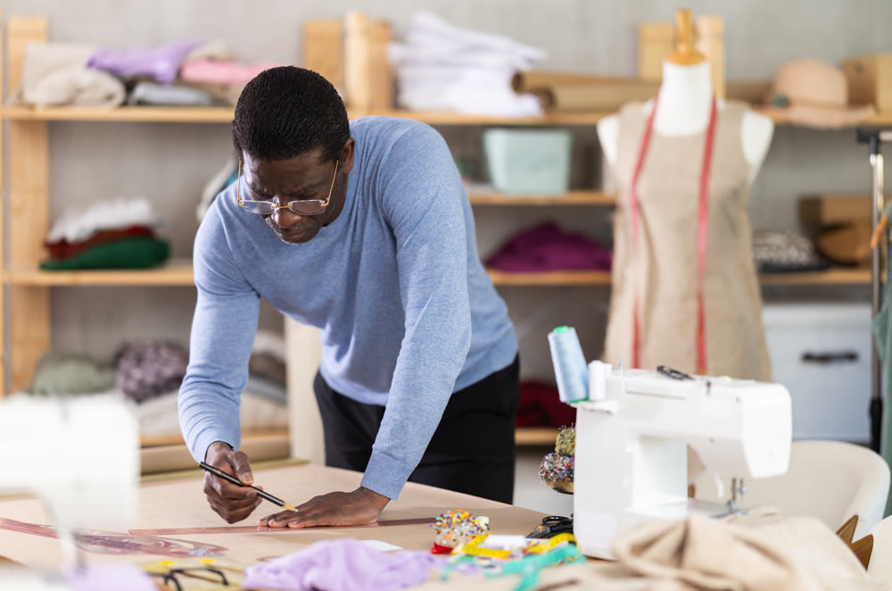 Middle-aged male dressmaker sketching clothing pattern in sewing workshop