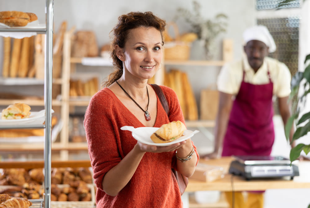Happy female customer tries delicious bocadillo in bakery interior