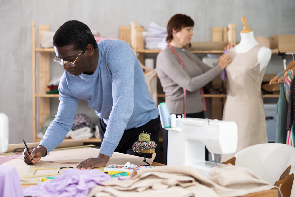 Male fashion designer drafting clothing pattern in studio with female colleague