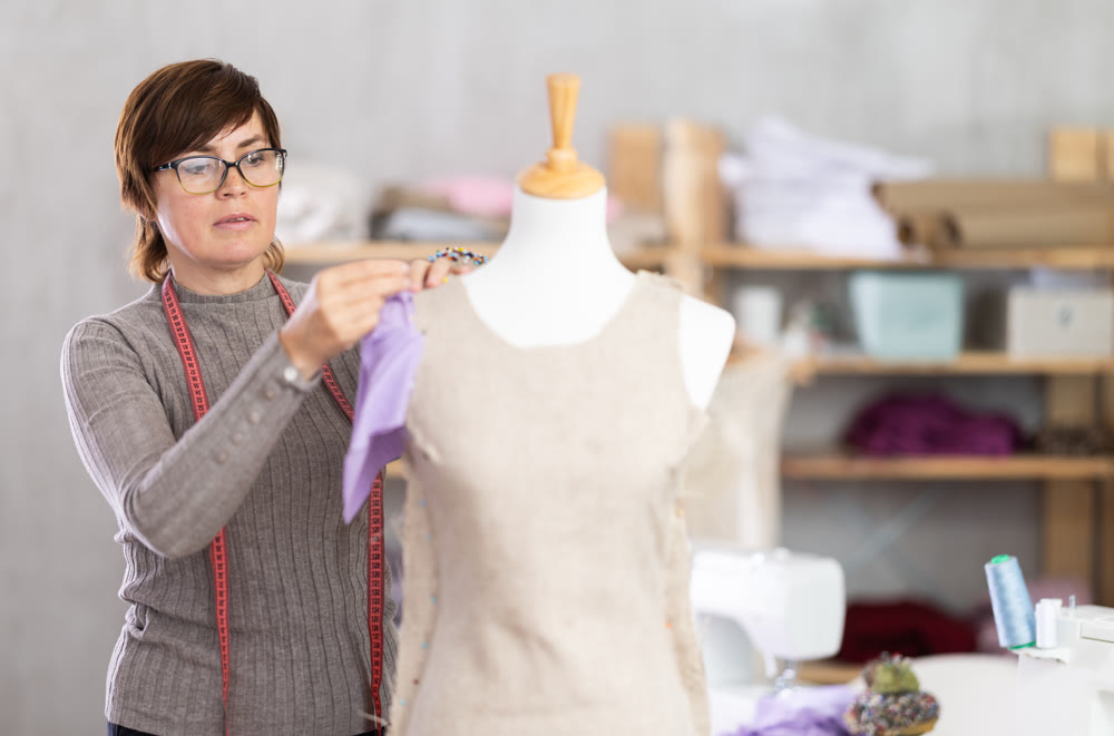 Woman tailor connects parts of dress on mannequin.