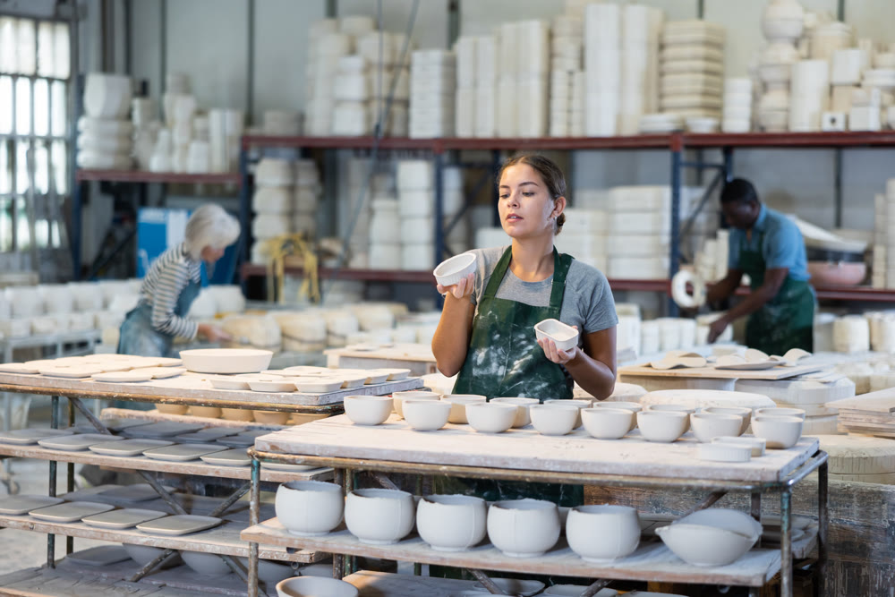 Girl ceramist arranging new bowls in workshop