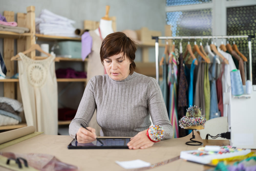 Female tailor draws sketch of future clothing on an electronic tablet. Working with modern gadgets in sewing workshop