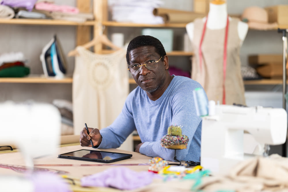 Male tailor draws sketch of future clothing on an electronic tablet. Working with modern gadgets in sewing workshop