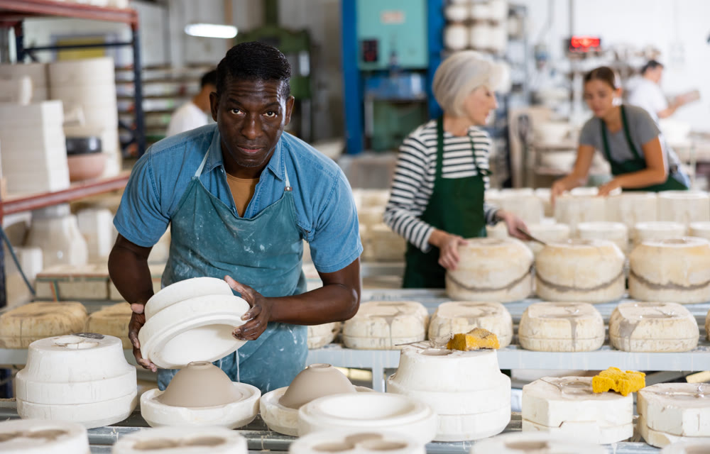 African american worker in pottery factory removes the first half of plaster mold from clay bowl