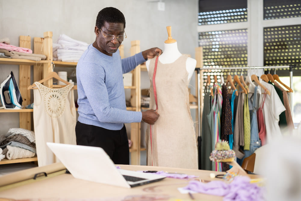 Male tailor sews new dress on a mannequin in sewing studio
