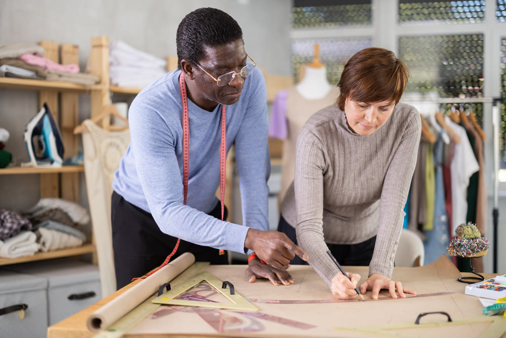 Two sewing workshop workers draw patterns on paper