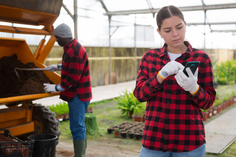 Young woman writing a message on the phone during break from work in greenhouse