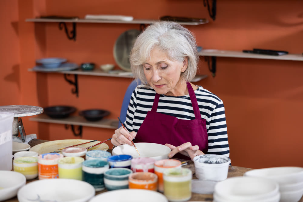 Mature craftswoman painting clay plates acrylic paints in art studio