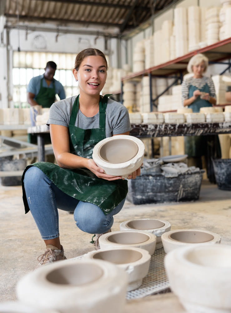 Positive young worker demonstrates half of plaster mold for pottery in pottery factory