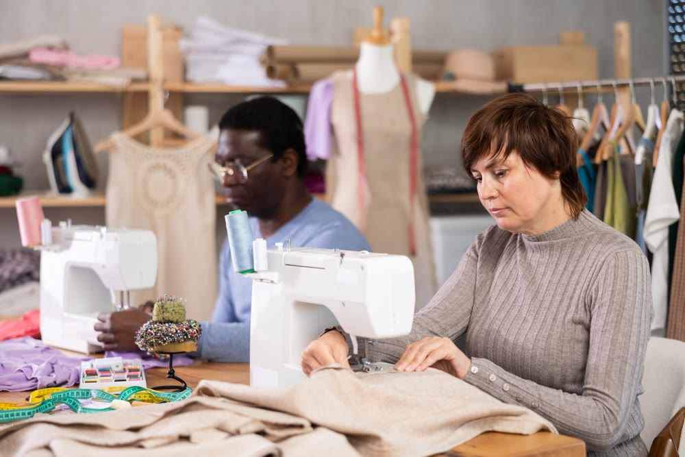 Working in sewing workshop - man and woman working at sewing machines, creating new clothes