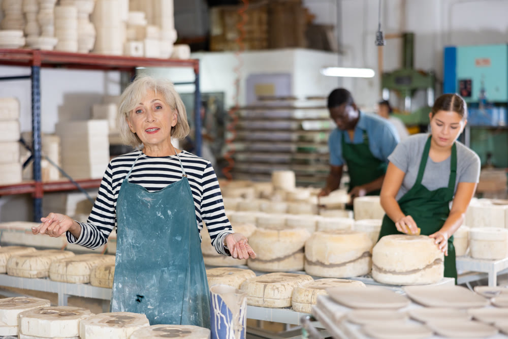 Portrait of an elderly craftswoman among ceramic plates and cups in the workshop of pottery factory