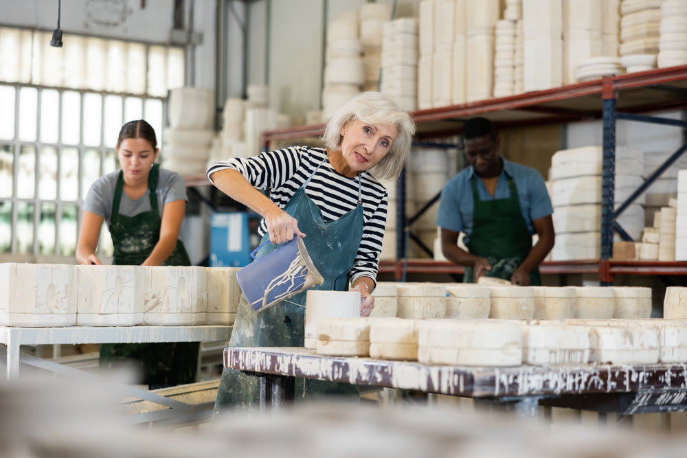 Mature worker pours slip mass from jug into plaster mold in pottery factory