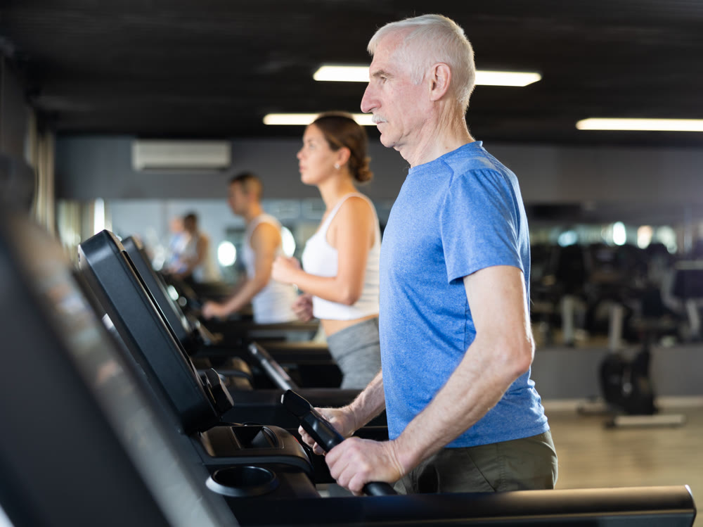 Portrait of elderly man running on treadmill in sport gym