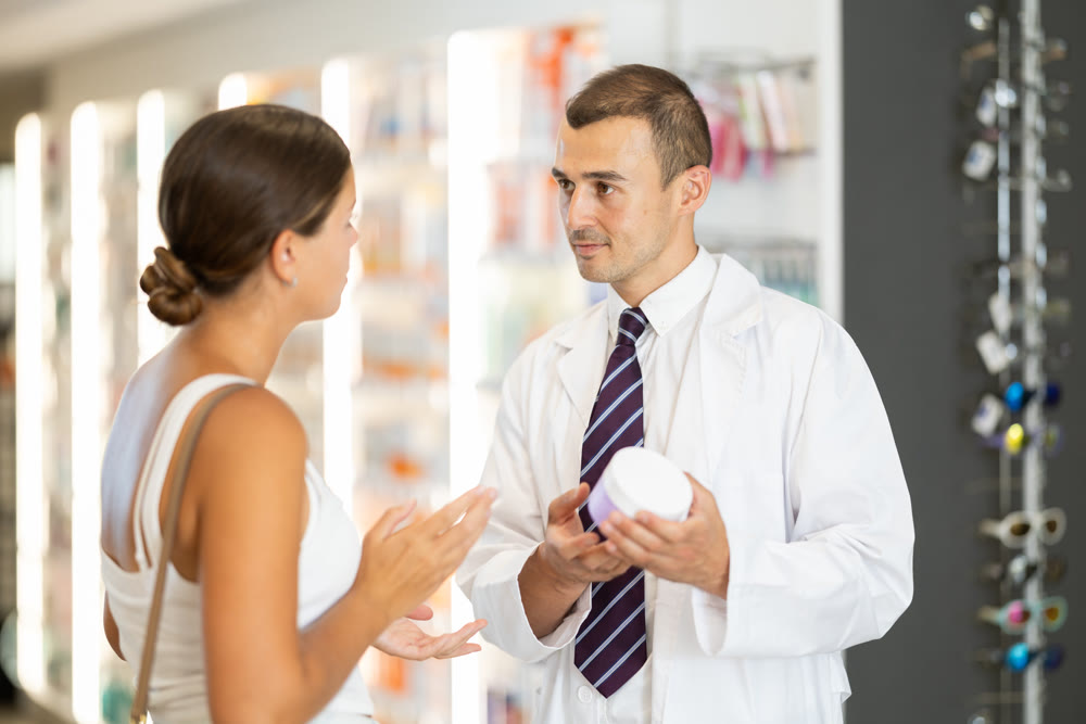 Male pharmacist consulting young girl about cosmetic cream
