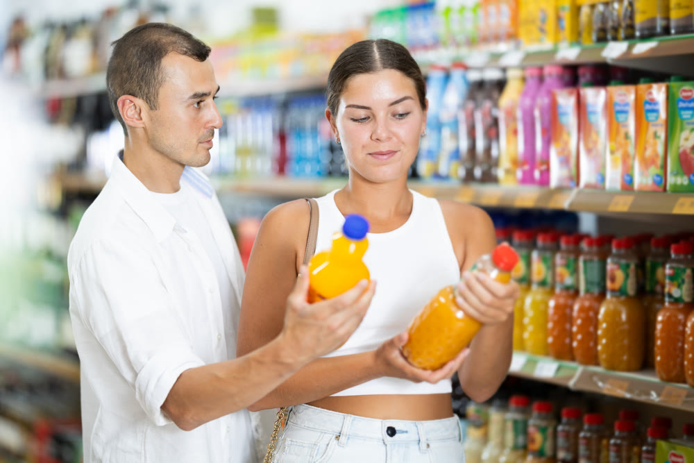 Positive couple choosing juice or soda while standing near glass display cases full of products in supermarket