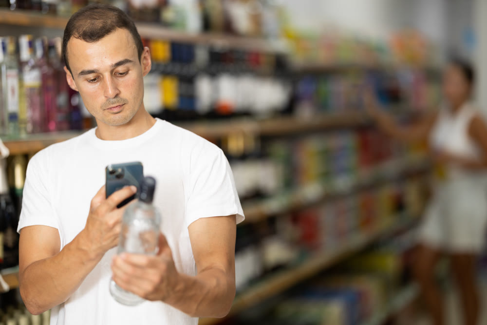 Man using smartphones to scan barcodes on bottles of alcoholic beverages