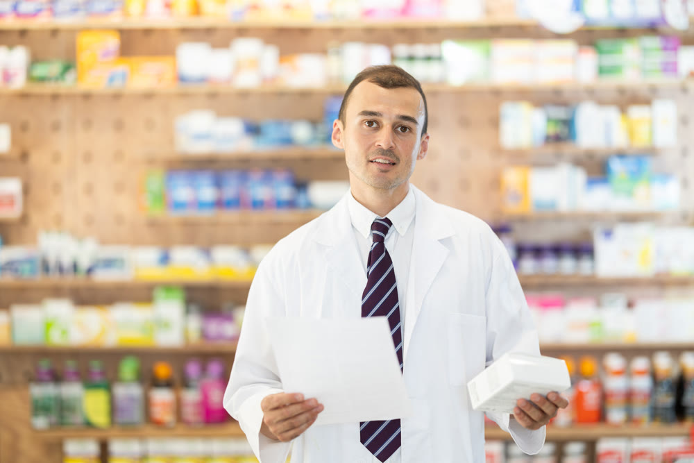 Young male pharmacist standing in drugstore with medicament and recipe in hands