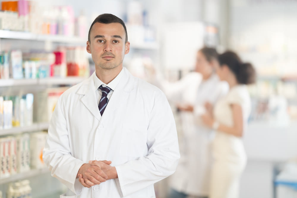 Positive male pharmacist in medical uniform posing while working in pharmacy